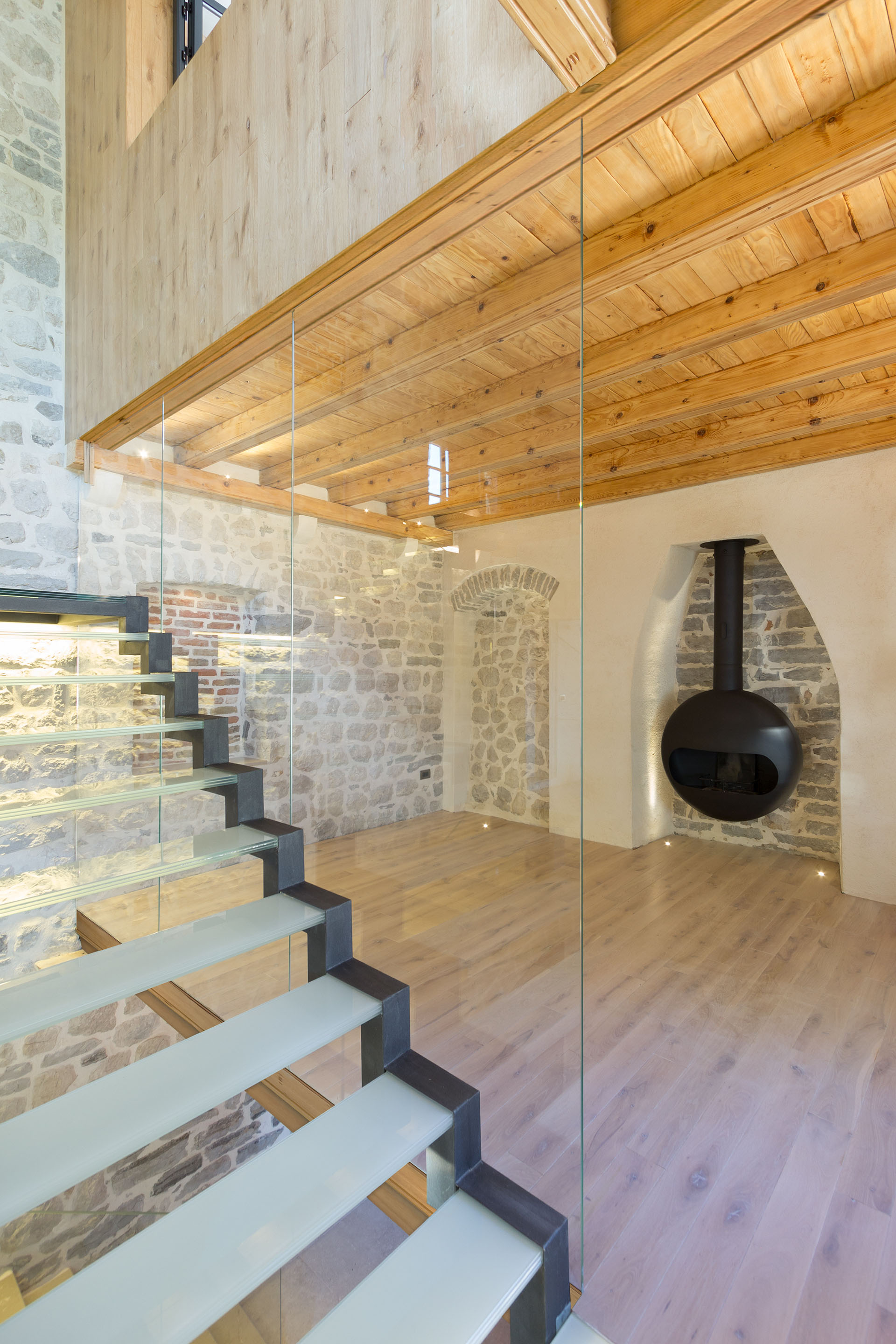 Living Room with Stone Walls, Fireplace, Natural Wood Floor and Glass Stairs